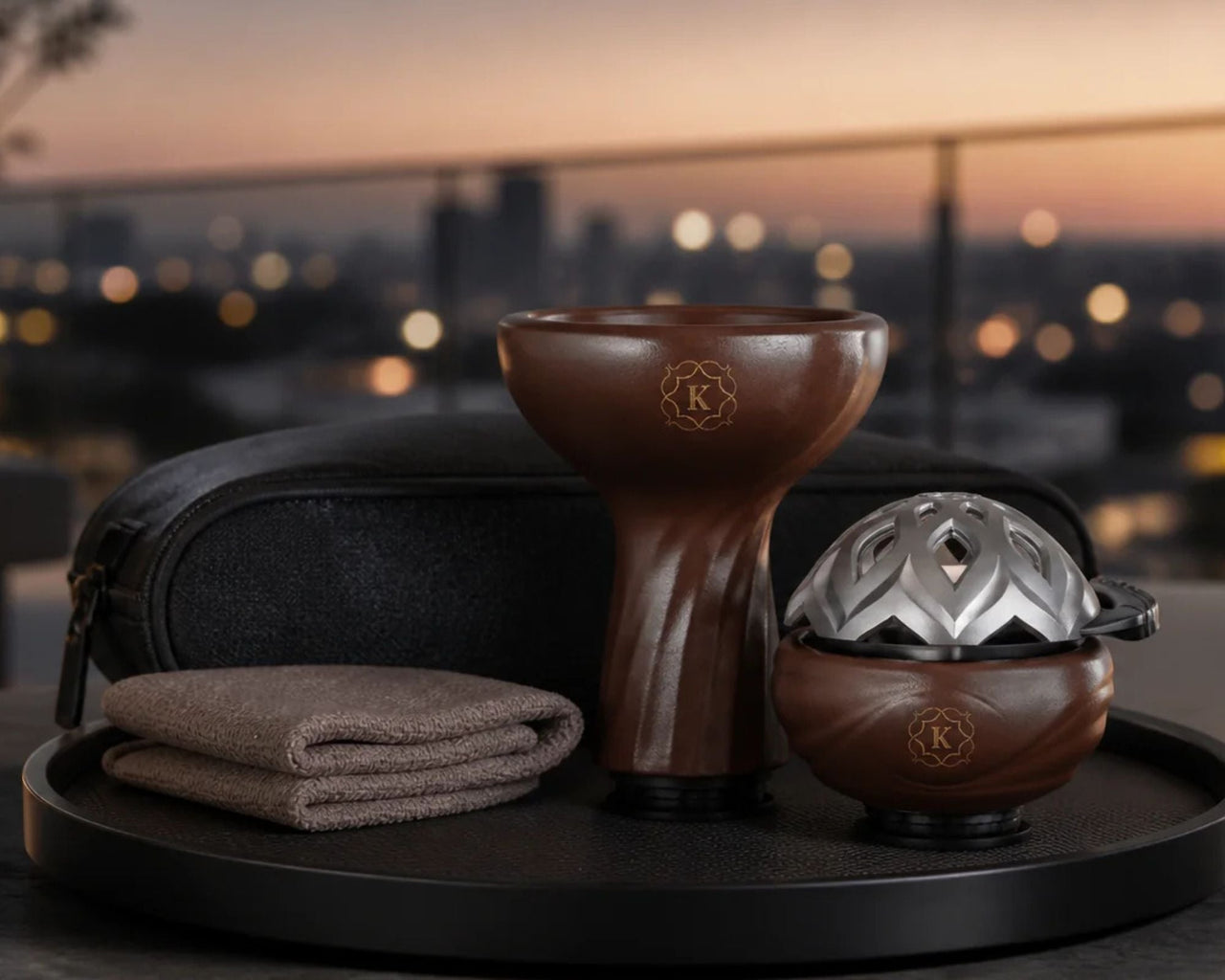 Kaloud Samsaris bowl in swirled brown ceramic beside a silver Lotus HMD lid, travel case, and cloth, set on a rooftop at sunset