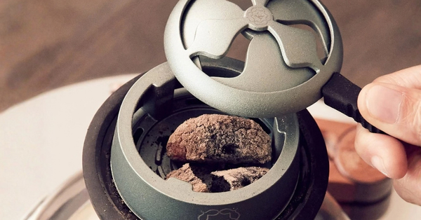 Kaloud Lotus heat management device with its vented lid lifted, showing lit charcoal held above the shisha in the hookah bowl